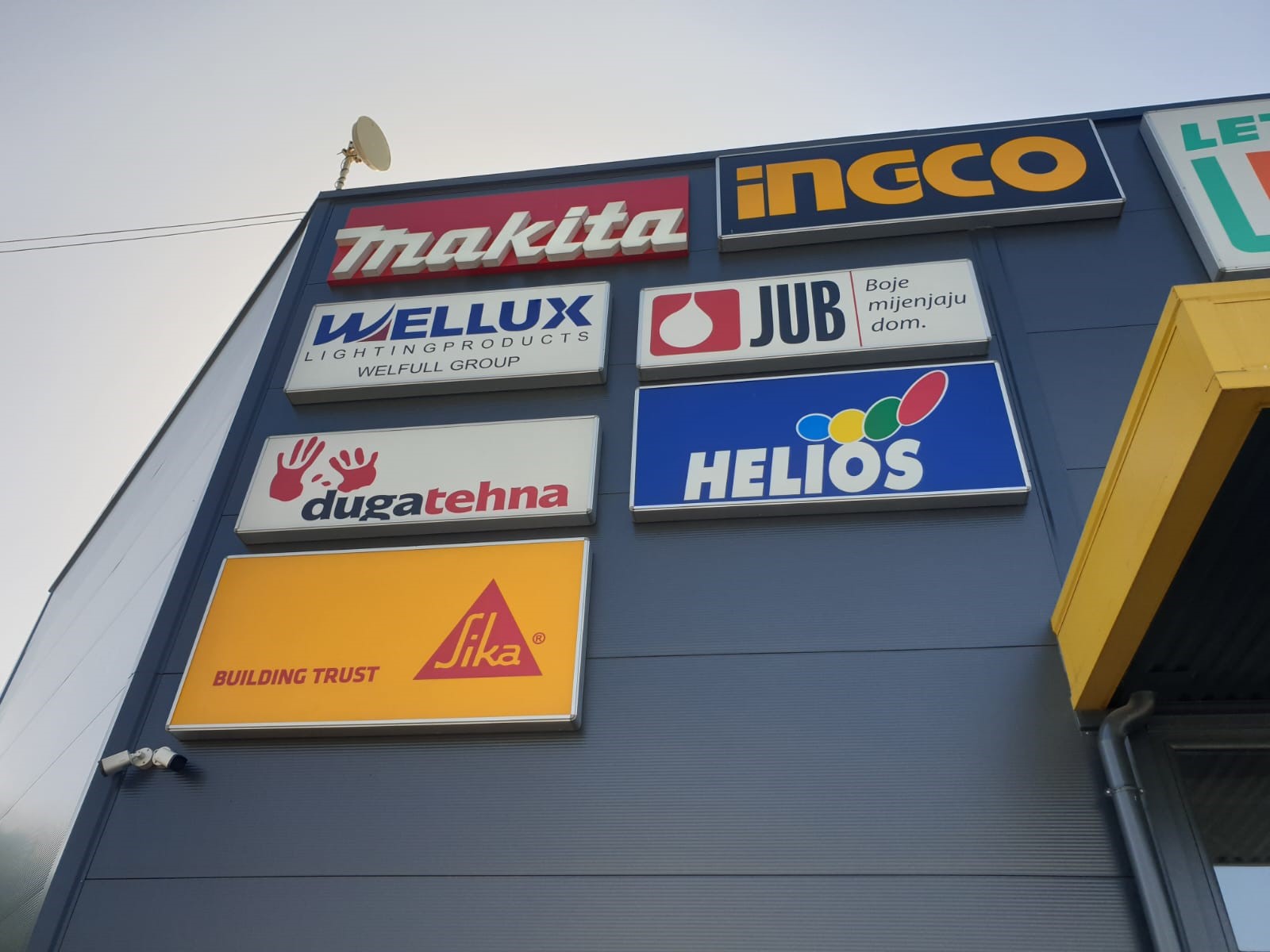 Niz svjetlećih kutija sa logotipima Makita, INGCO, Wellux, JUB, Helios i Sika na fasadi objekta