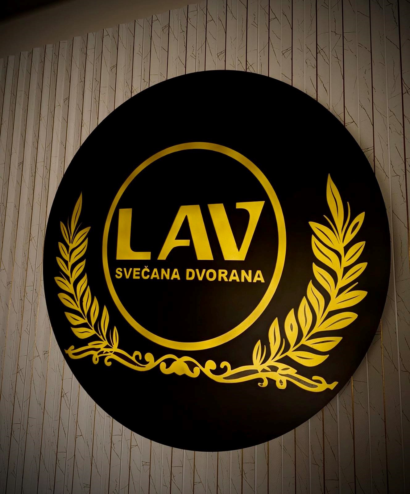 Okrugli svjetleći logo LAV svečane dvorane, crno-zlatna izvedba na zidu